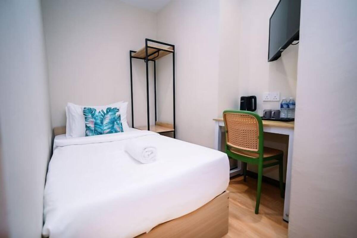A compact hotel room with a single bed, a desk with a chair, a flat-screen TV, and a coffee maker.