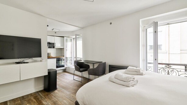 Habitación de hotel moderna con una cama grande, televisión de pantalla plana, pequeña cocina y balcón con vistas.
