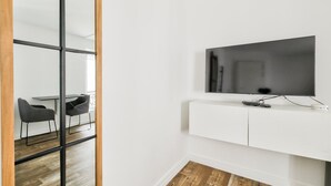 Una sala moderna con un televisor de pantalla plana montado en una pared blanca, una puerta corredera con marco de madera y un comedor con mesa y sillas.
