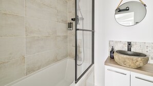 Un baño con ducha de vidrio, un espejo redondo y un lavabo de piedra.