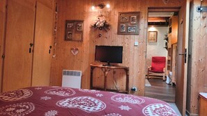 A wooden-paneled room with a bed, a television on a wooden stand, and a red chair.