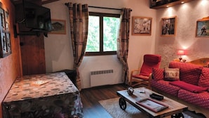 A cozy room with a wooden table, a red sofa, and a window with curtains.