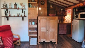 A cozy room with a wooden cabinet, a red chair, and a kitchen area with a microwave and refrigerator.