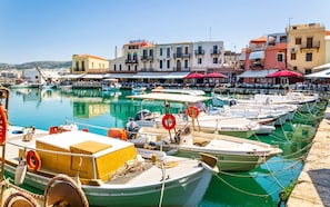 A marina with boats docked, a waterfront promenade, and buildings with balconies.