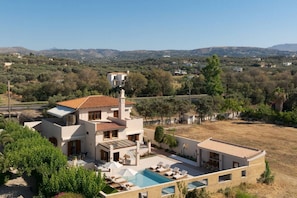 A modern villa with a swimming pool, multiple rooms, and a view of the surrounding landscape.