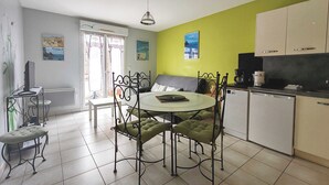 Ein Essbereich mit einem runden Tisch, vier Stühlen, einer kleinen Küchenzeile inklusive Schränken, einem Kühlschrank und einem Fenster mit Vorhängen.