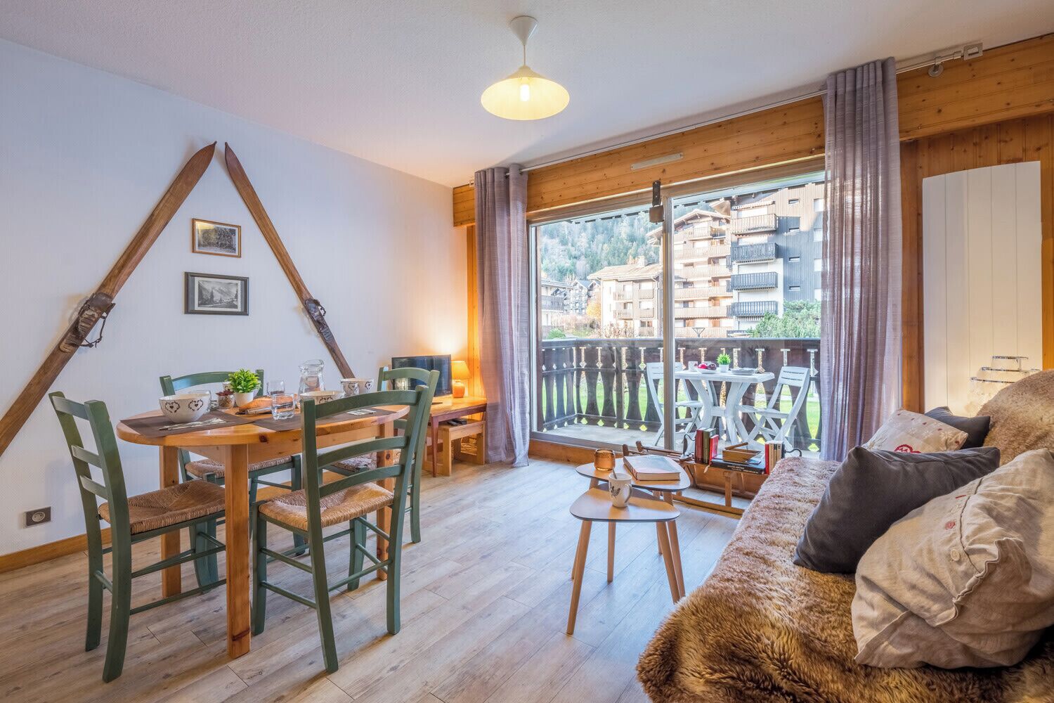 A cozy living room with a dining area, wooden furniture, and a balcony with a view of buildings.