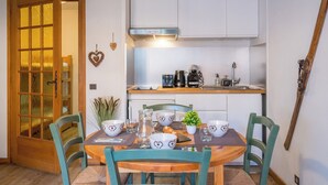 Une cuisine de taille réduite avec des meubles blancs, une table à manger en bois et des chaises de couleur turquoise.