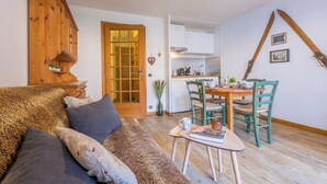 Un salon chaleureux avec un meuble en bois, un canapé avec des coussins, une table à manger avec des chaises et un coin cuisine équipé d’une cuisinière et de placards.