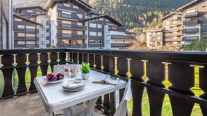 Un balcon avec une table dressée pour le dîner, donnant sur une région montagneuse parsemée d’immeubles à plusieurs étages.