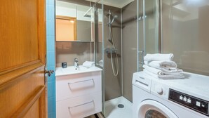 Une salle de bain moderne dotée d’une douche à parois de verre, d’un lave-linge encastré et d’un meuble-lavabo avec miroir.