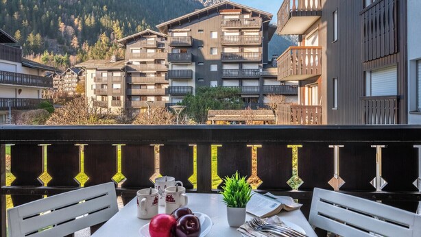 Un balcon avec une table préparée pour le petit-déjeuner, d’où l’on peut admirer une montagne et des immeubles d’habitation.