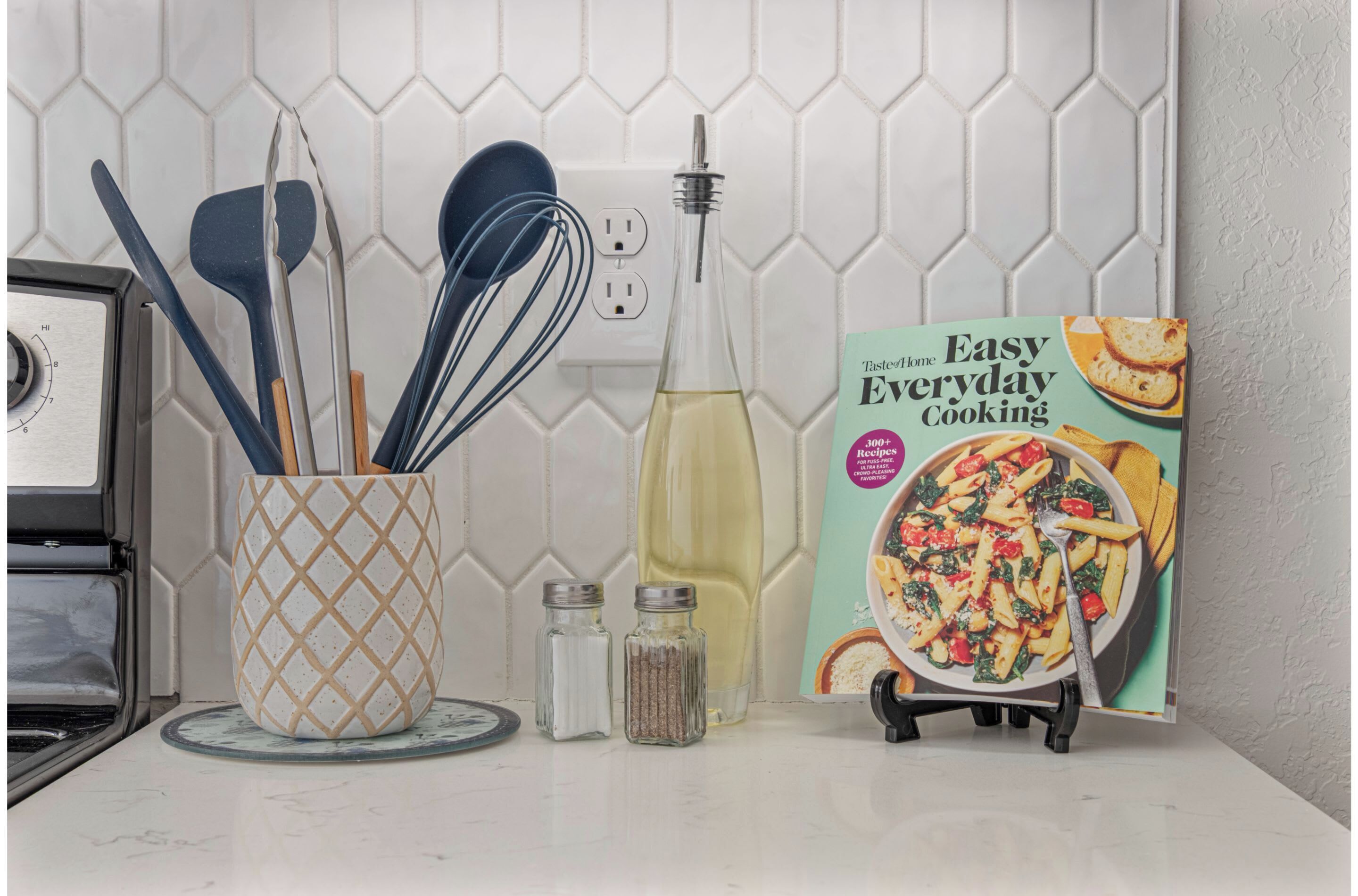 Una encimera de cocina con utensilios, una botella de aceite, saleros y pimenteros, y un libro de cocina titulado 'Easy Everyday Cooking'.