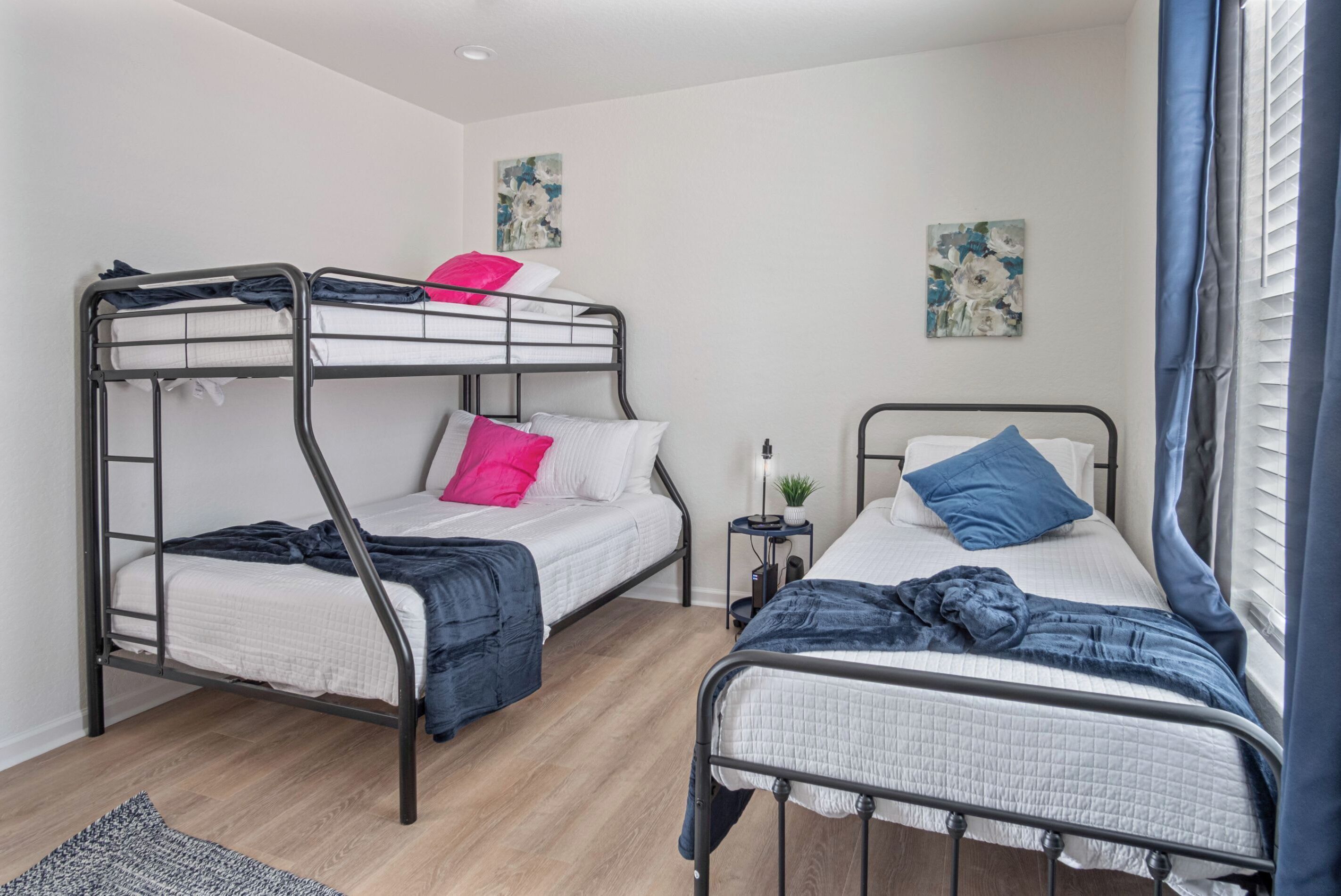 Un dormitorio con literas, una mesita de noche pequeña con lámpara, y dos cuadros colgados en la pared.