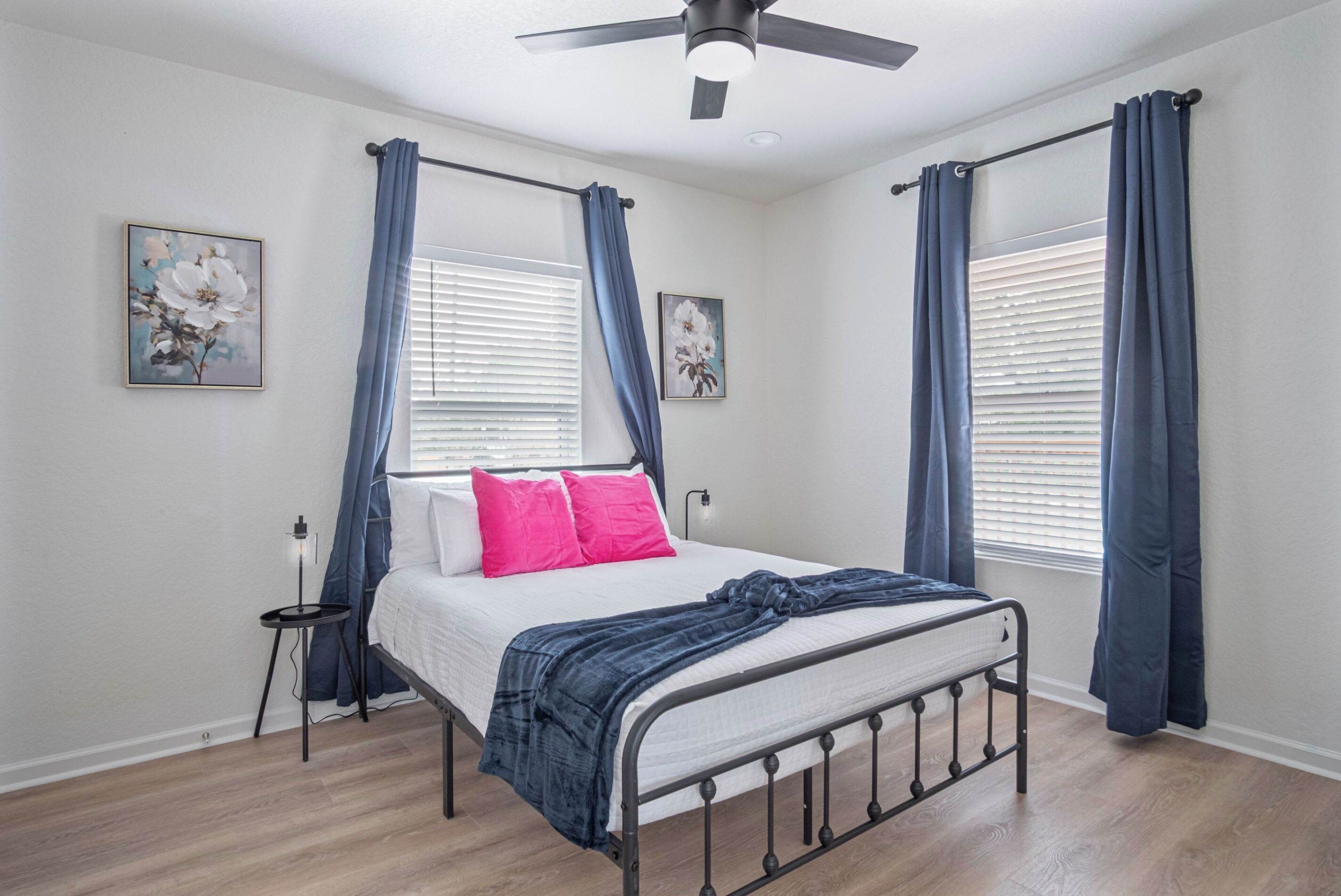 Un dormitorio con cama, ventilador de techo y dos ventanas con cortinas.