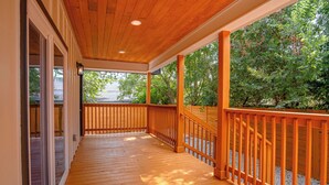 A covered wooden deck with a railing, leading to a glass door.