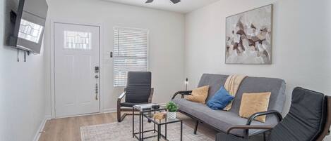 A living room with a ceiling fan, a gray sofa with cushions, a black chair, and a coffee table with a plant.