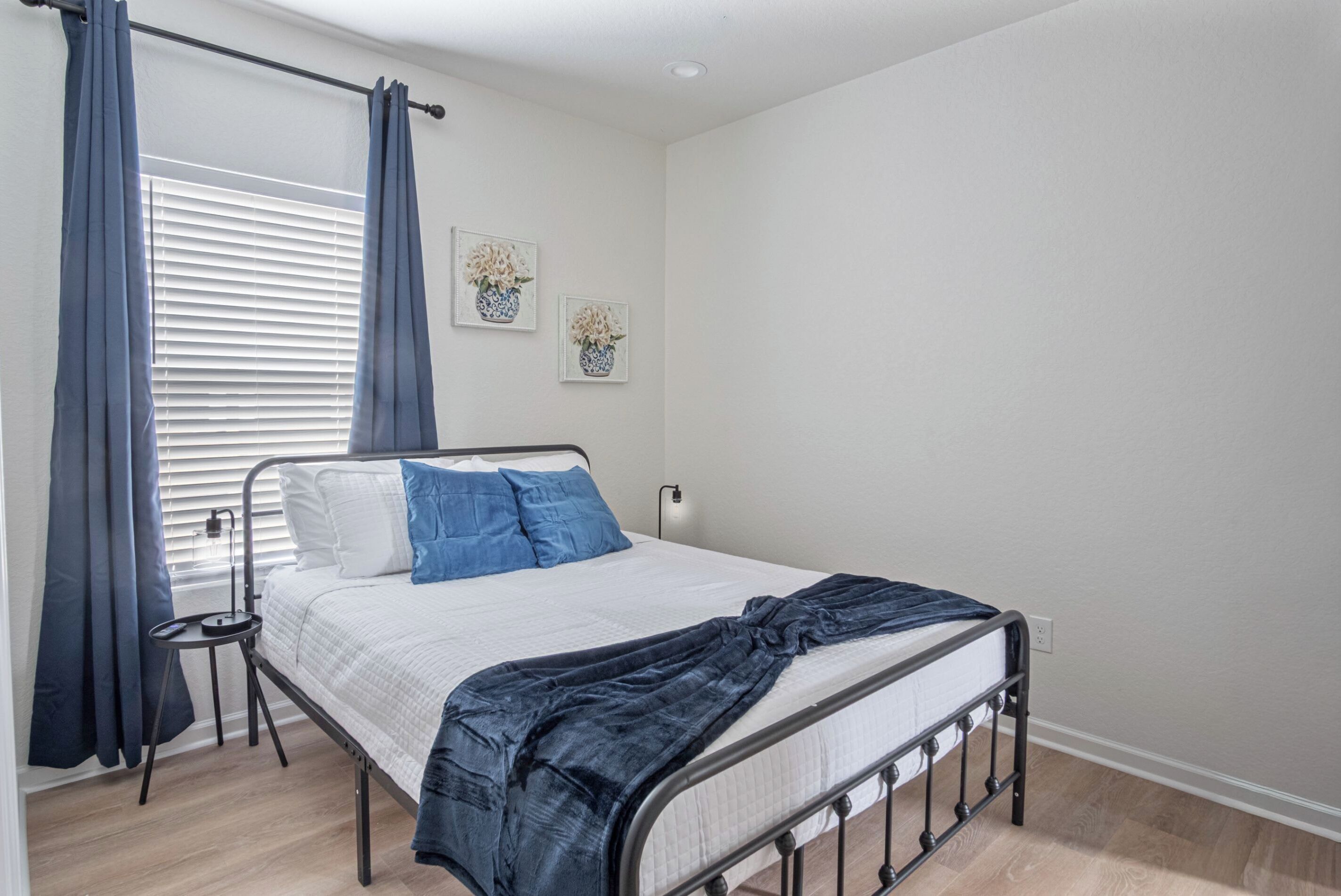 A bedroom with a bed, curtains, a bedside table, and wall art.