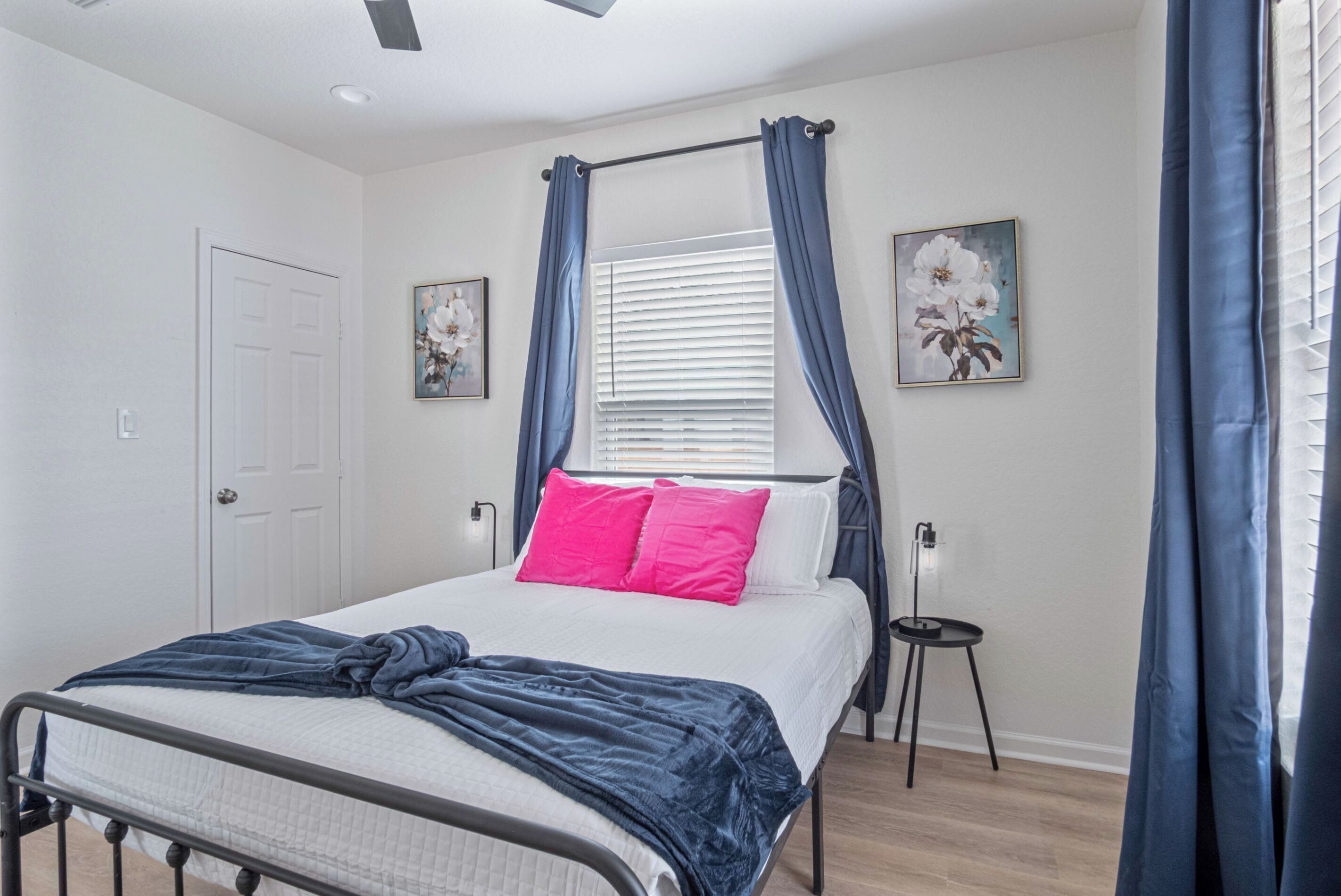 A bedroom with a bed, a window with curtains, a door, and two wall-mounted paintings.