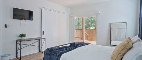 A bedroom with a bed, a desk, a TV, and a sliding door to a balcony.