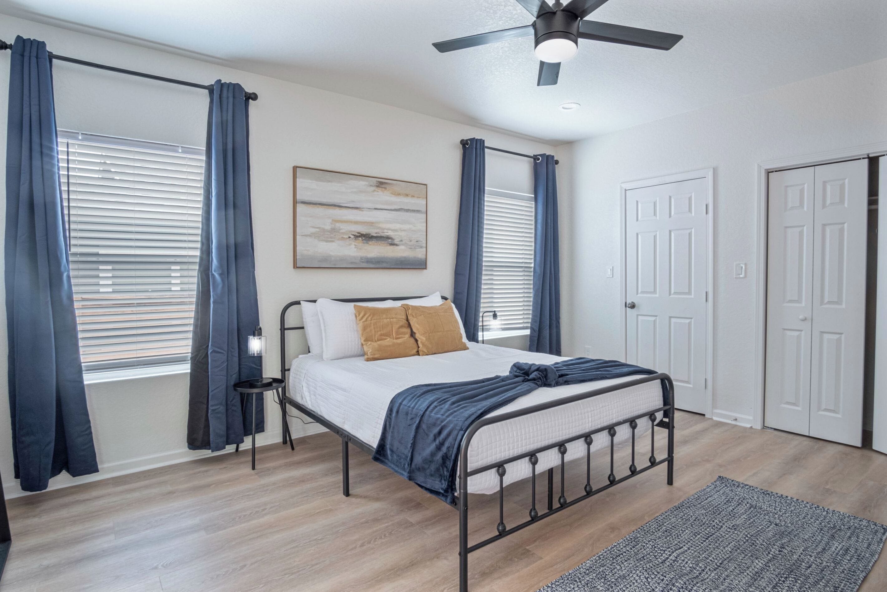 Une chambre à coucher avec un lit, un ventilateur de plafond, une fenêtre avec des rideaux et une porte.