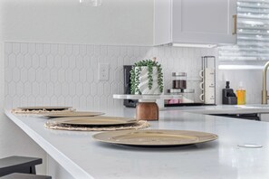 A modern kitchen with white cabinetry, a marble countertop, and a decorative plant centerpiece.