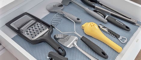 A drawer with various kitchen utensils including a grater, spatula, and a yellow peeler.