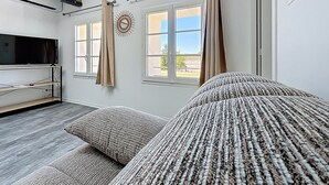 Un salon moderne avec un grand téléviseur à écran plat, un canapé et une fenêtre avec des rideaux.