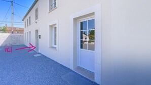 Un bâtiment blanc doté de nombreuses fenêtres et d’une porte. Une zone pavée se trouve devant le bâtiment.