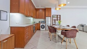 A modern kitchen with wooden cabinets, a built-in washing machine, and a dining area with a table and chairs. - 3 beds Pratamnak Near Walking Street (Chon Buri)