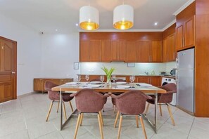 Une cuisine moderne avec des meubles en bois, un réfrigérateur en acier inoxydable et un coin repas avec une table dressée pour quatre personnes.