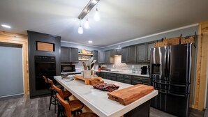 Una cocina moderna con una isla central, armarios oscuros, electrodomésticos de acero inoxidable y taburetes de madera.