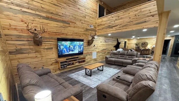 Una sala de estar moderna con paredes de madera, un televisor de pantalla plana, sofás de cuero y una mesa de centro de madera.