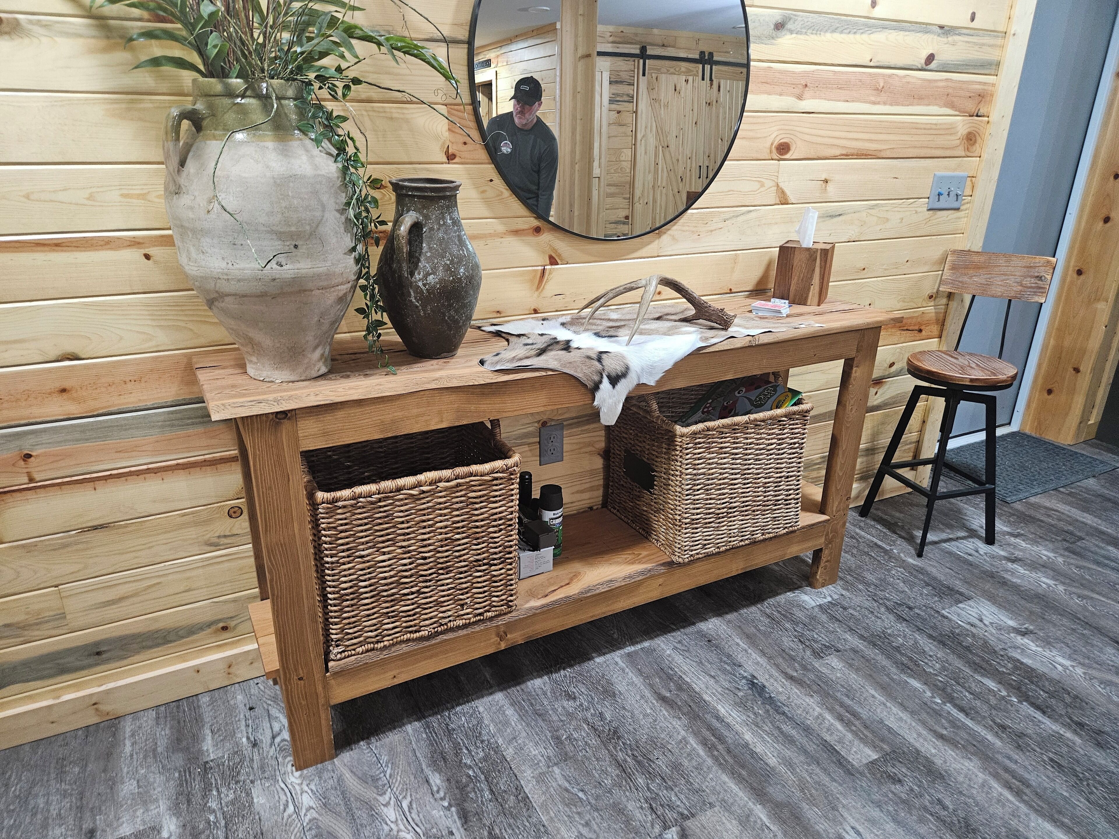 A wooden vanity with a mirror, two wicker baskets, and a vase with a plant.
