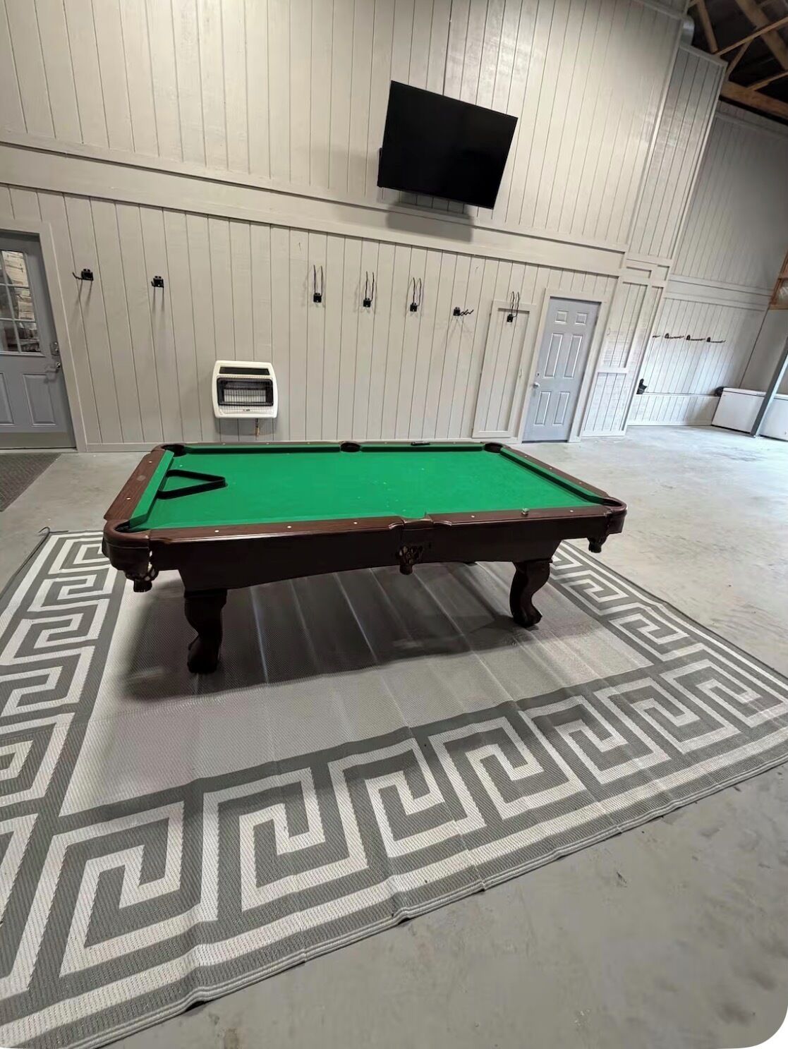 A pool table with a green felt surface, a geometric-patterned rug, and a television mounted on the wall.