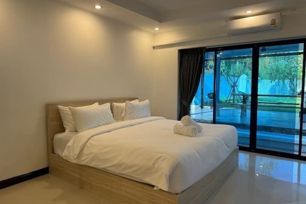 A modern hotel room with a large bed, a glass door leading to a balcony, and a ceiling-mounted air conditioning unit.