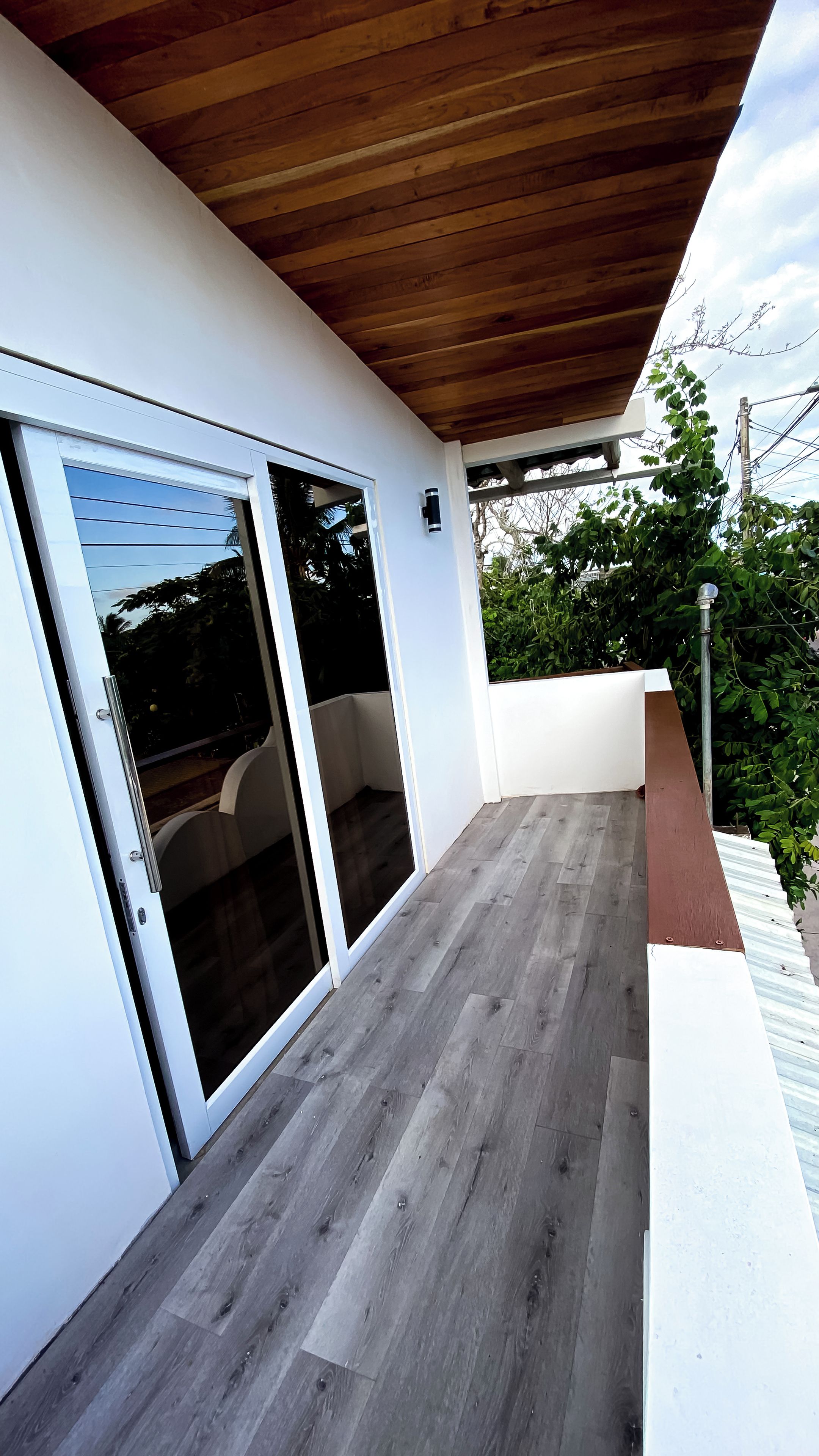 Un espacio al aire libre techado con techo de madera, puerta corrediza de vidrio y pared blanca.