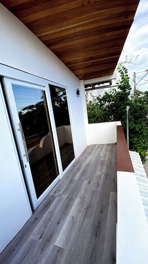 Un espacio al aire libre techado con techo de madera, puerta corrediza de vidrio y pared blanca.