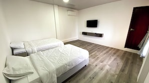 Un dormitorio con dos camas, un televisor montado y suelo de madera.