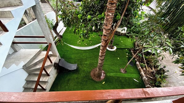 A rooftop garden with a hammock, palm trees, and a staircase.