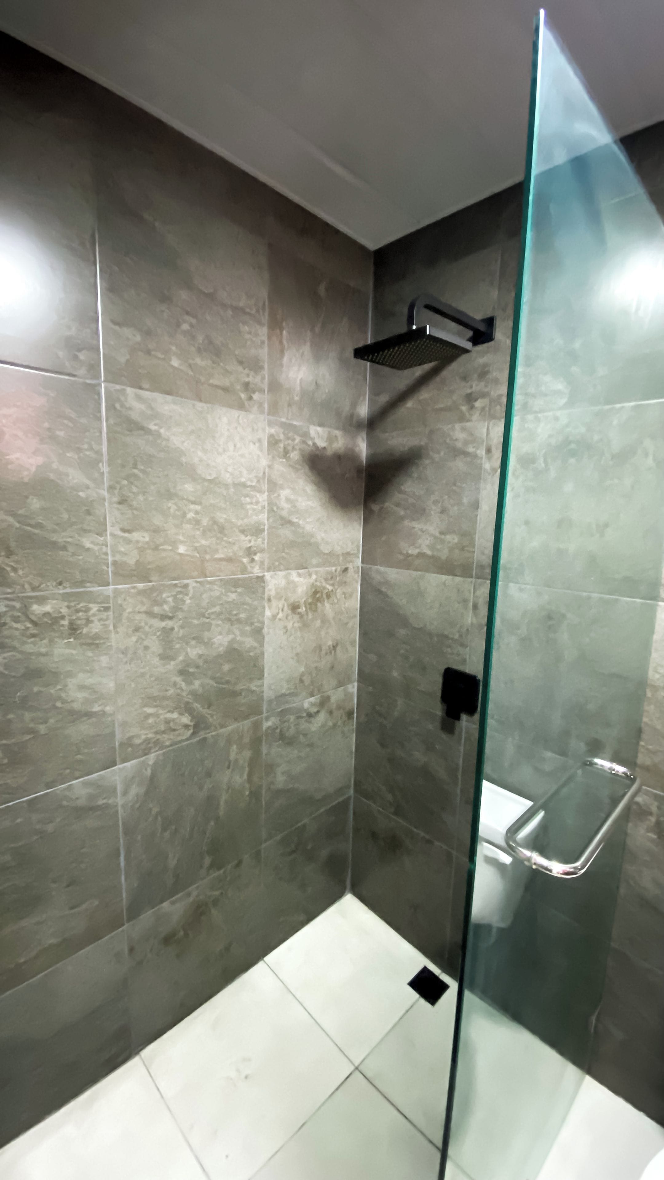 Une salle de bain moderne avec une douche à parois de verre, un porte-serviettes noir et un lavabo blanc.
