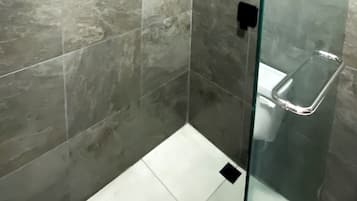 Een moderne badkamer met een glazen douchecabine, een zwarte handdoekhouder en een witte wasbak.