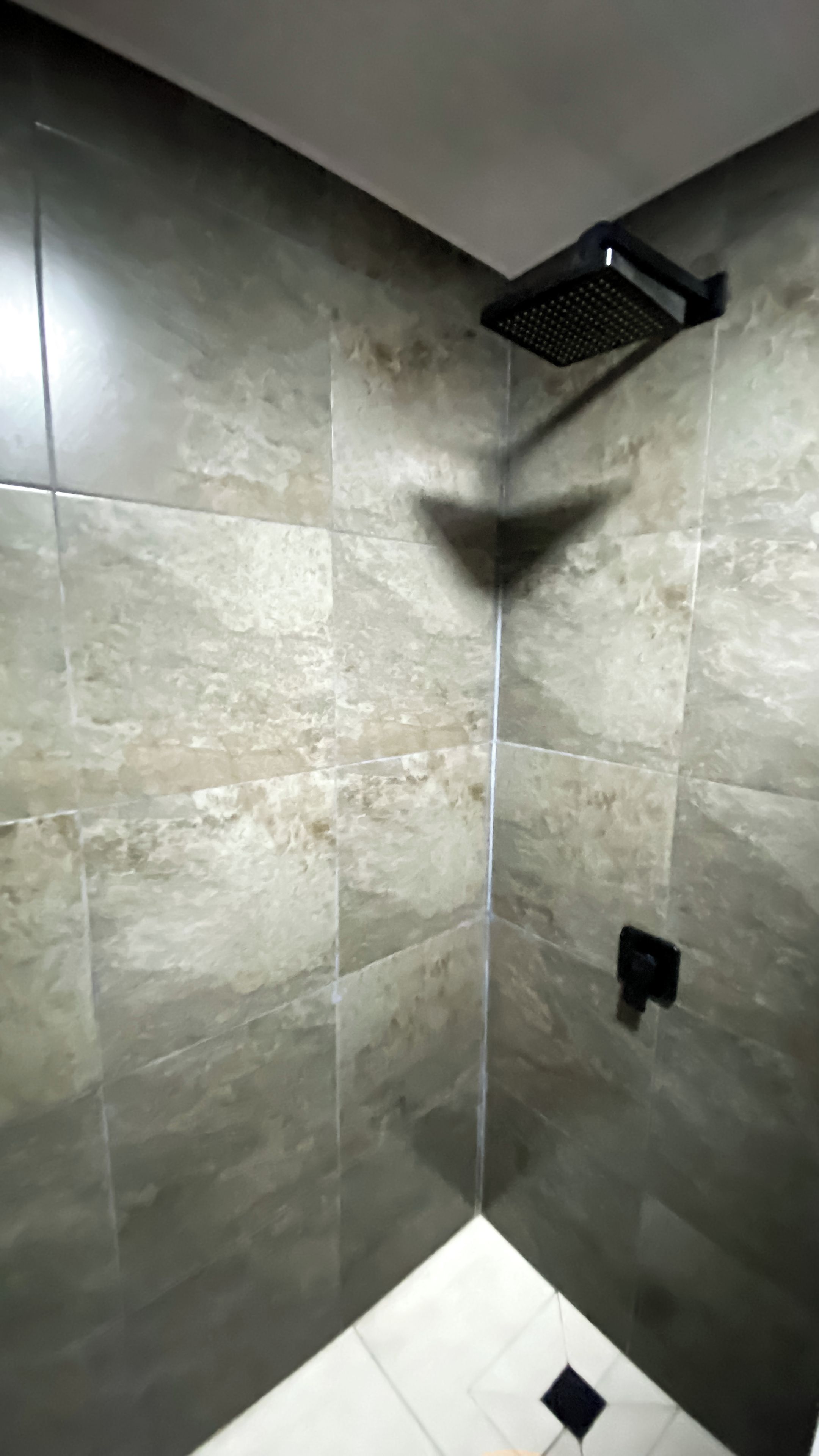 A shower area with a corner showerhead and tiled walls.