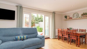 Ein Wohnzimmer mit grauem Sofa, einem Esstisch mit Holzstühlen und einem an der Wand befestigten Fernseher.
