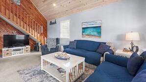 Een woonkamer met een blauwe bank, een witte salontafel, een flatscreen televisie en een houten plafond.