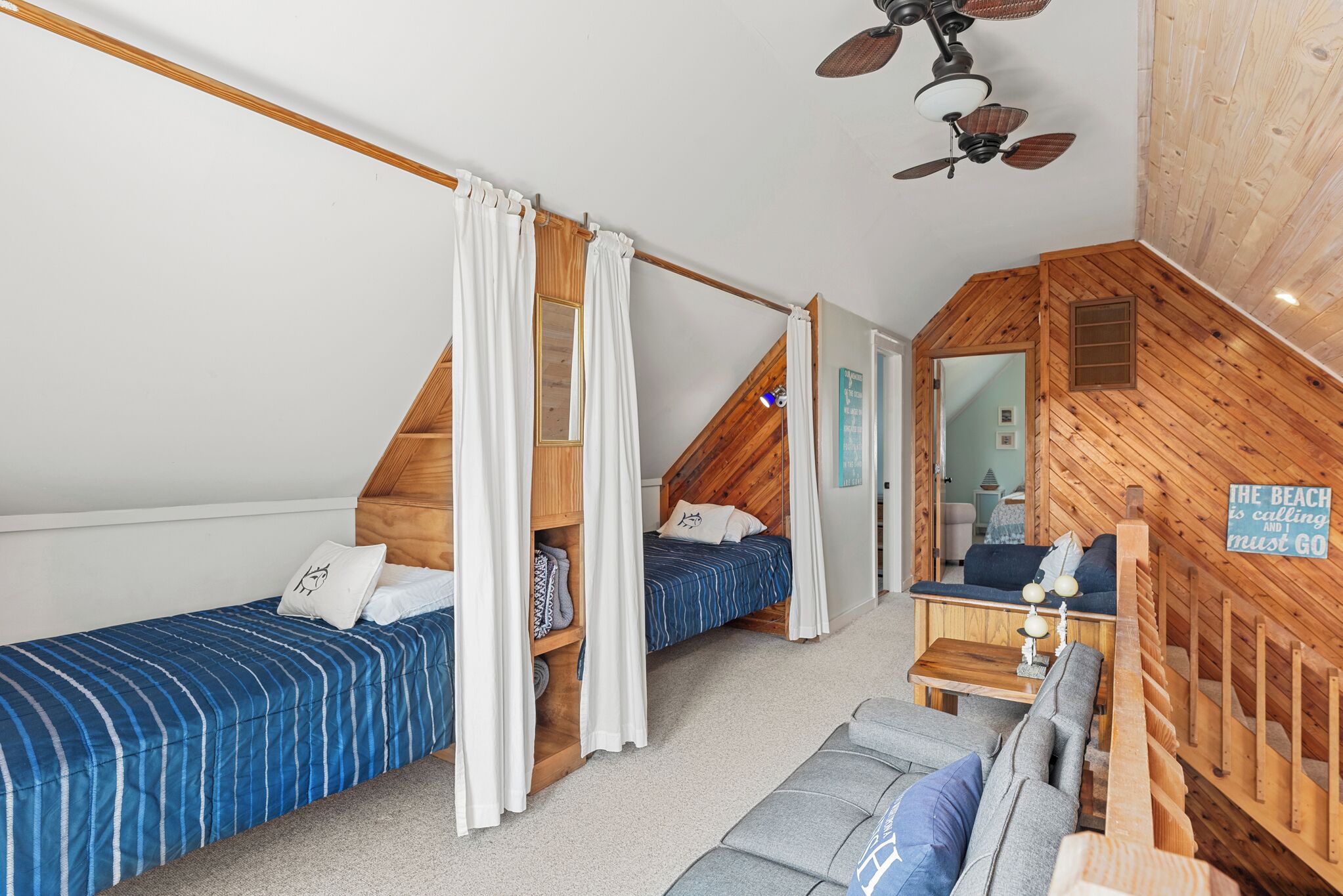 Une chambre mansardée chaleureuse avec deux lits, un plafond en bois et un petit coin salon.
