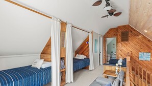 Een knus slaapkamer op zolder met twee bedden, een houten plafond en een klein zitgedeelte.