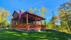 A wooden cabin with a porch, surrounded by trees and a clear sky.