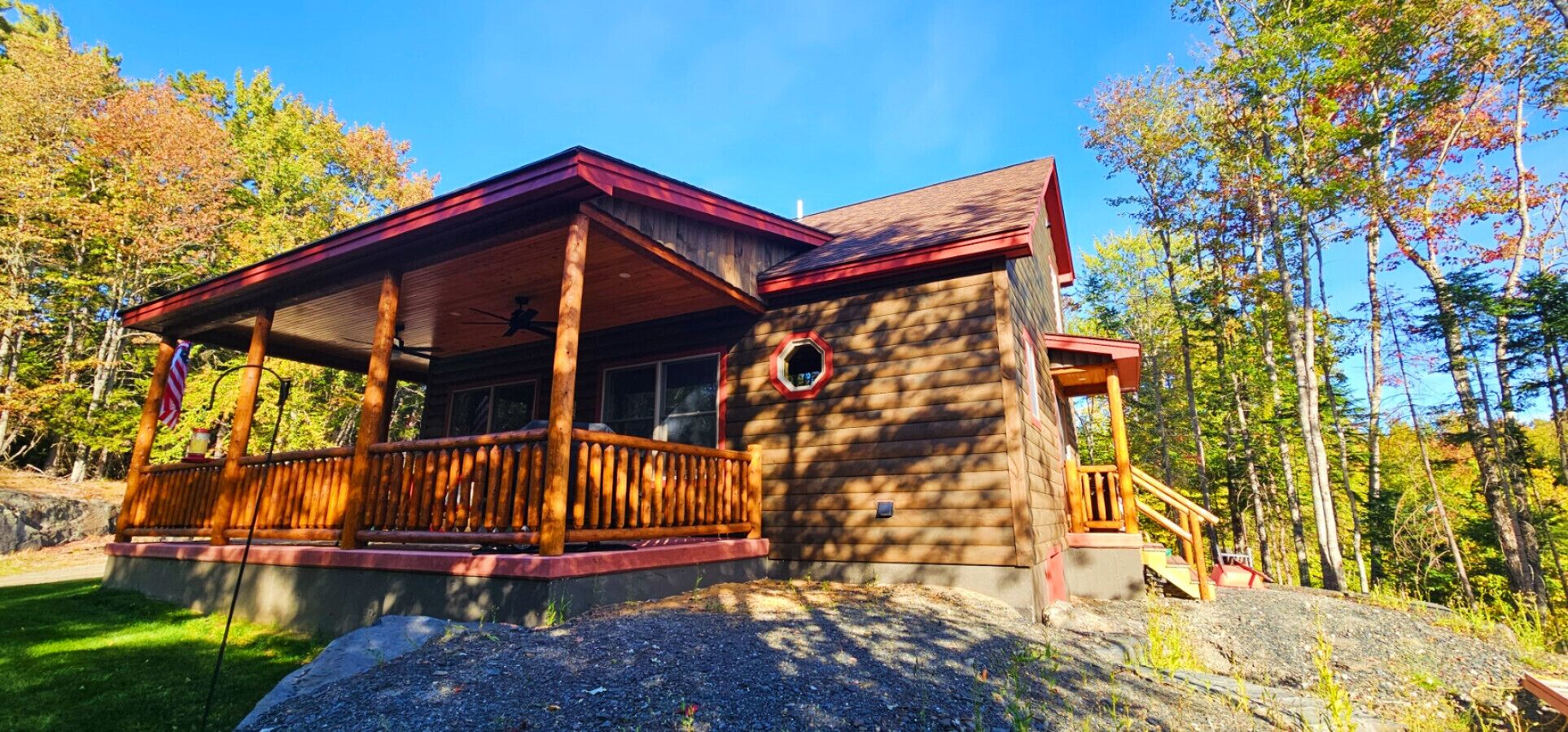 Une cabane dotée d’un porche en bois, d’une terrasse couverte et de fondations en pierre.