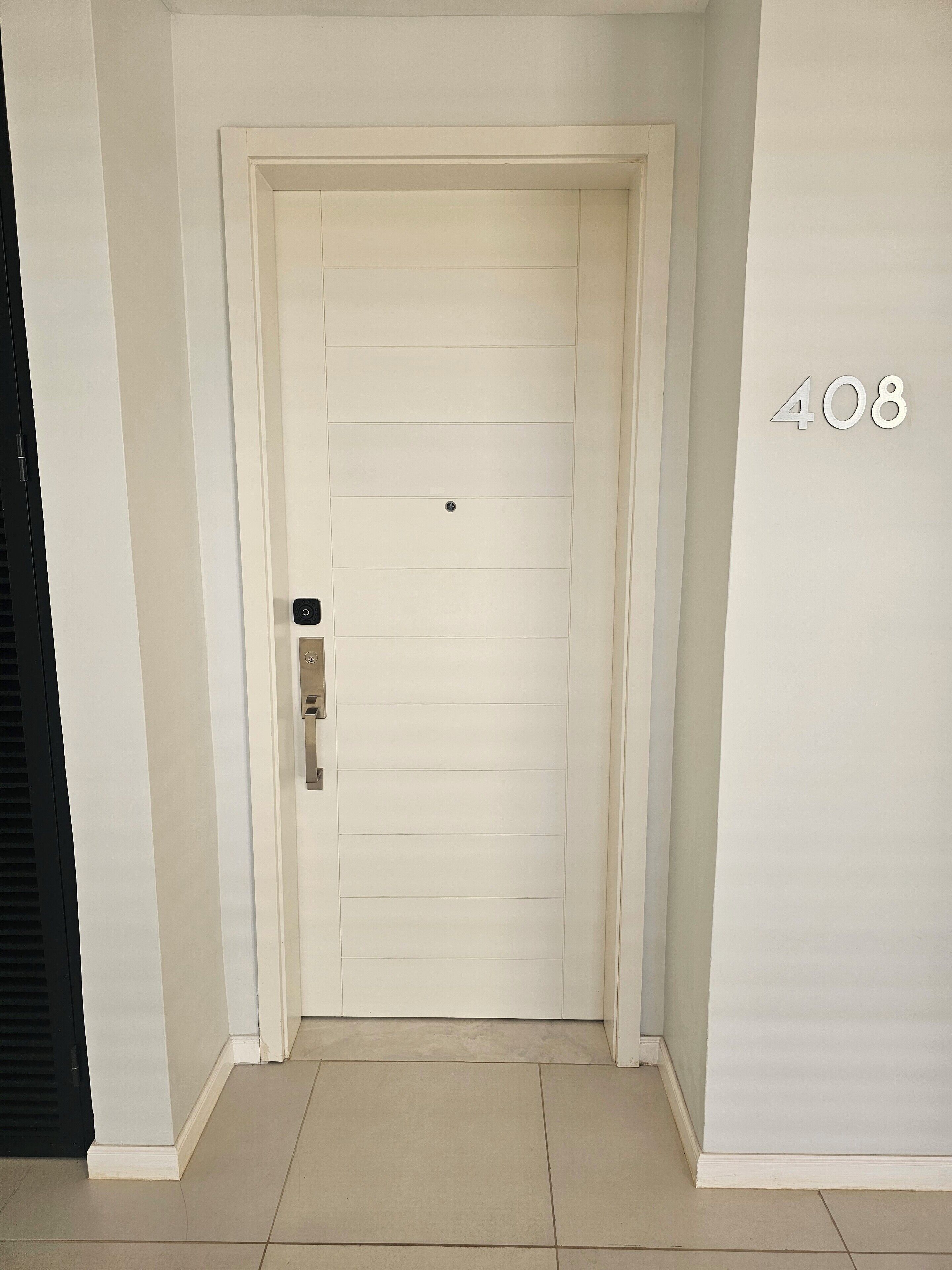 A white door with a numeric keypad lock, a doorbell, and a number '408' on the adjacent wall.